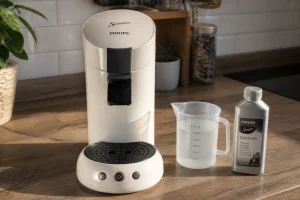 Machine à café Senseo blanche en cours de détartrage avec récipient gradué sur plan de travail