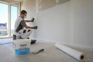 Artisan posant de la toile de verre sur un mur avec masque et gants de protection
