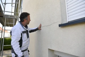 Artisan examinant une fissure sur une façade avec isolation thermique par l'extérieur
